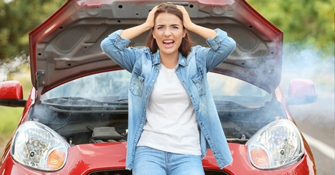 worried young girl holding her head in hands is standing infront of her red car that got out of order.