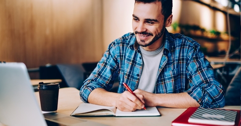 male student making notes from laptop