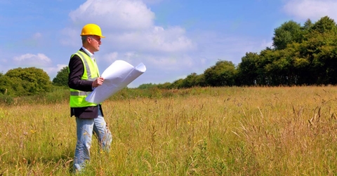 An architect in construction gear surving a new building plot.