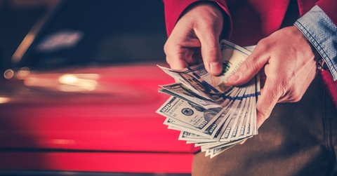 man counting money over vintage car
