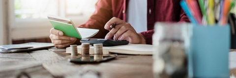 man calculating finances at table woth stack of coins and calculator