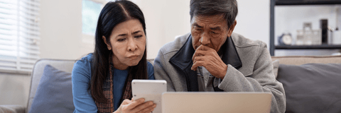 stressed senior couple looking worried at bills on computer