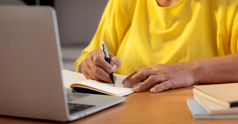 Senior woman writing note at desk with laptop