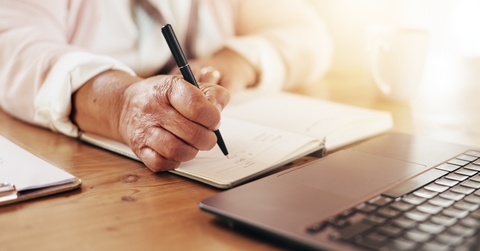 senior person writing notes and using laptop for planning