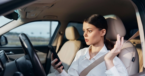 a woman holding a phone in a drivers seat look surprised
