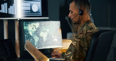 Military analyst wearing headset evaluating charts