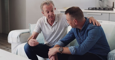 Older father sitting on couch having a serious conversation with his adult son