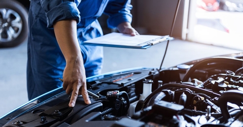 mechanic with a clipboard checking a car engine