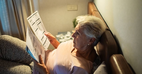 Worried senior woman reading bills in bed at night 