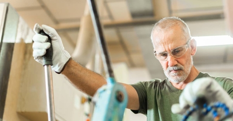 Older worker threading a steel bar in an industrial factory