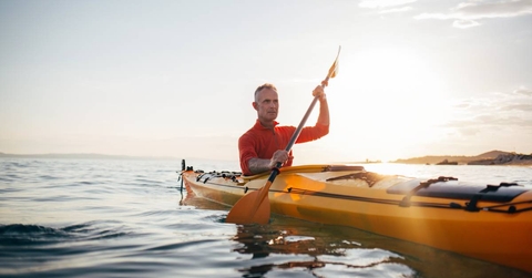 Senior man paddling kayak during sunset
