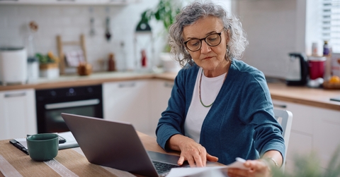 senior woman analyzing documents while using laptop