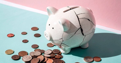 Cracked piggy bank with scattered coins on pastel background