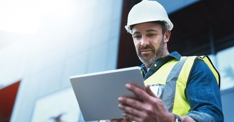 man with vest and hard hat looking at a tablet