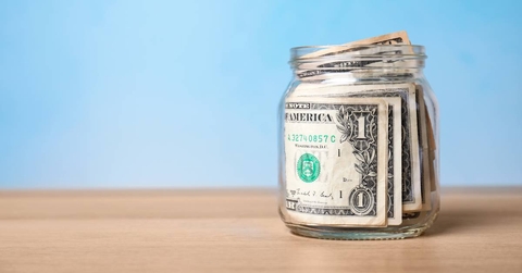Jar with money on table against color background