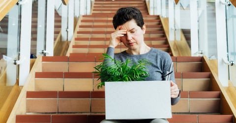 Woman with box of personal items sitting alone on the staircase after being laid off from job
