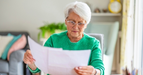 Older woman with white hair looking at paperwork worried