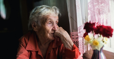Sad elderly woman looking out window
