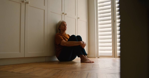 Sad Senior Woman Sitting On Floor At Home 