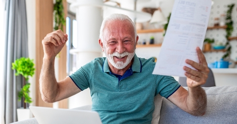 Older man happy smiling with arms up holding a paper