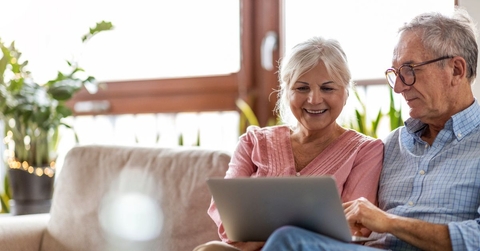 Smiling retired couple on the couch with laptop
