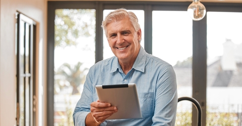 Man in his 60s smiling at the camera holding a tablet