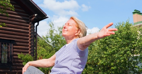 Woman sitting on the grass with open arms, enjoying the sunshine