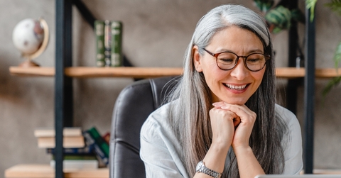 Woman in her 60s smiling in her office as she looks down 