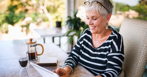 Woman with short, white hair sitting at the table reading a letter and having coffee
