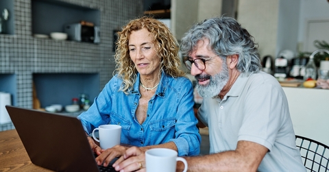 Couple in their 60s sitting at home having coffee and looking at notebook