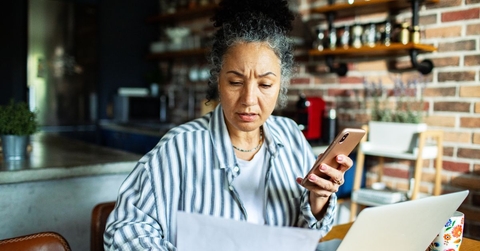 Mature woman on laptop and phone with worried expression