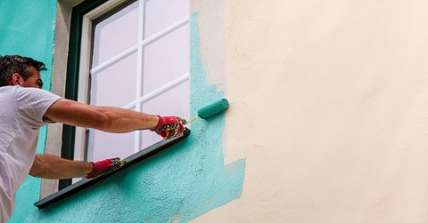 Man paints the facade walls of a house with paint using a paint roller 