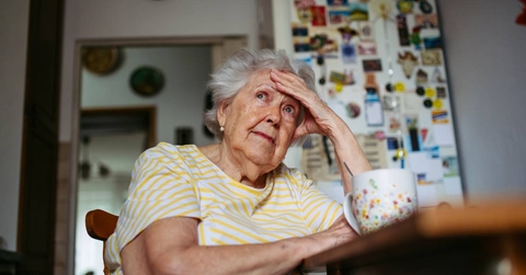 Portrait of worried senior woman sitting in kitchen. 