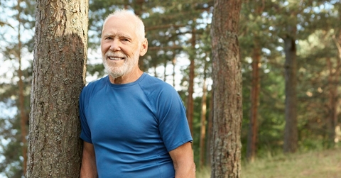 Smiling older man leaning against a tree