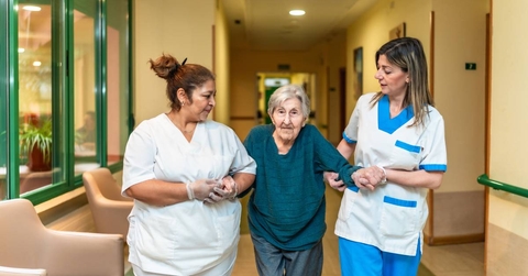Nurses helping elderly woman walking in nursing home corridor 