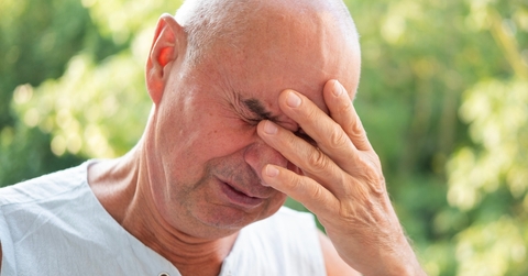 Man in his sixties looking worried with eyes closed and hand on his face