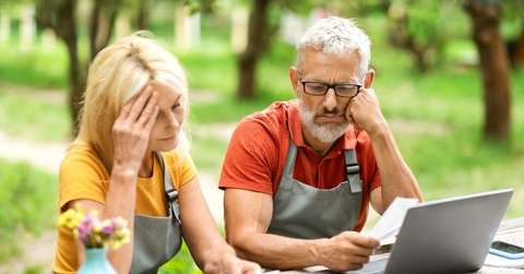 Retired couple sitting outside looking over finances worried faces