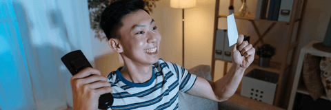 Young man watching tv with lottery ticket in hand