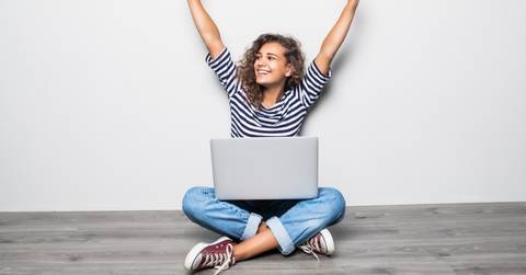 woman with laptop arms in air celebrating