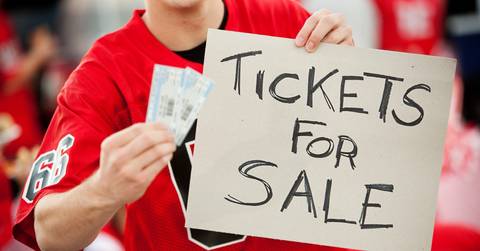 A sports fan holds two tickets and a sign that says &quot;Tickets for Sale.&quot;