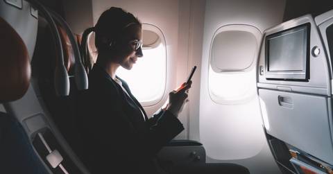 woman using smartphone sitting at window seat in airplane 